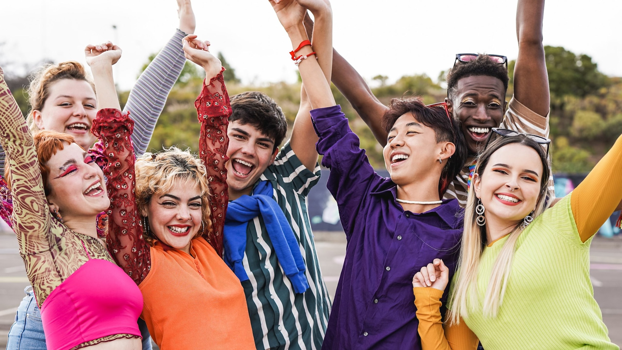 Multiracial LGBTQ+ students having fun together sitting outside school.