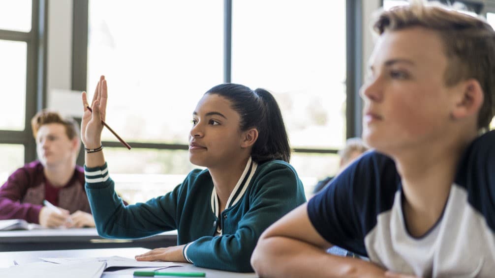 A female high school student raises her hands in classroom.