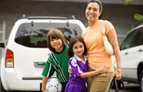 A mother with 2 happy kids in a school parking lot