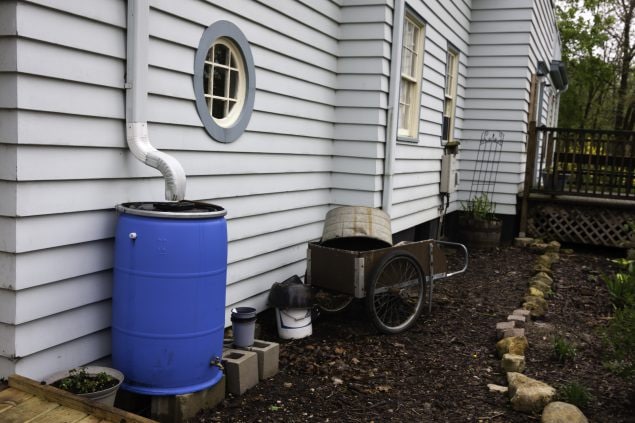 gran balde azul al lado de una casa recogiendo agua del desagüe de la casa