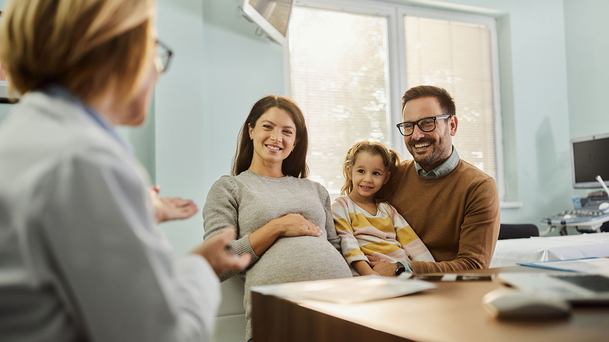 A happy pregnant woman and her family talking to a doctor during an appointment in the hospital.