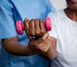 Midsection of nurse guiding senior woman in lifting dumbbell.