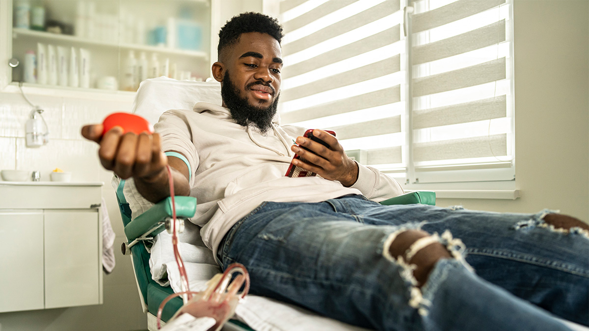 A man looking at his phone while giving blood in a doctor's office