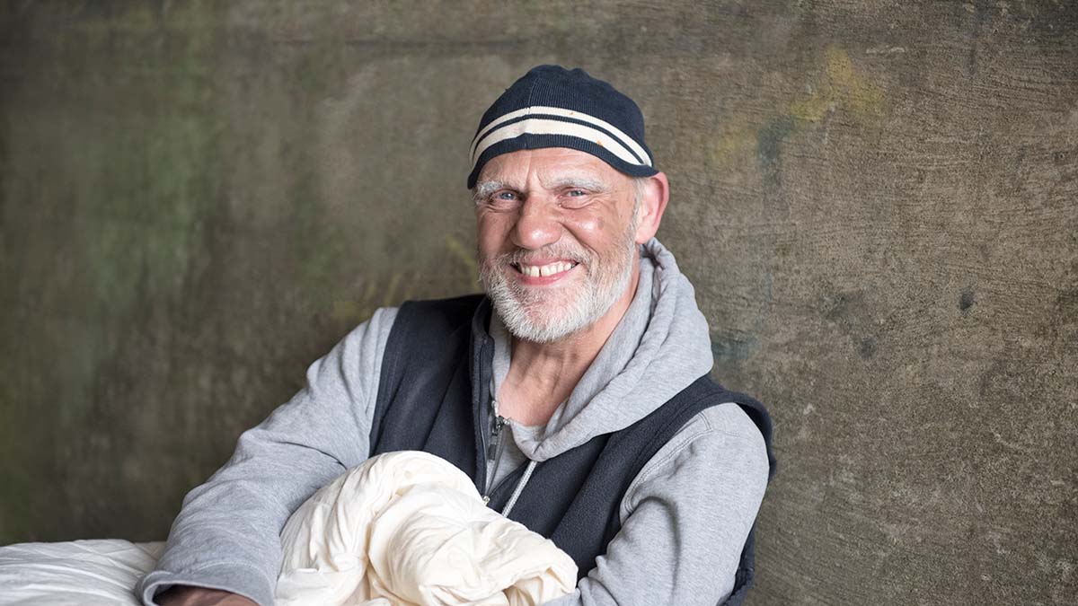 Person experiencing homelessness susceptible to viral hepatitis sits against a concrete wall with a blanket