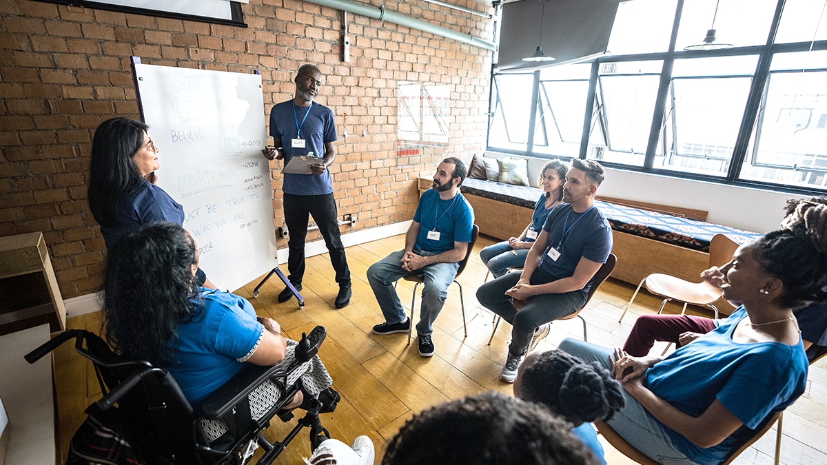 A diverse group of people sitting in a circle while a moderator presents on a whiteboard.