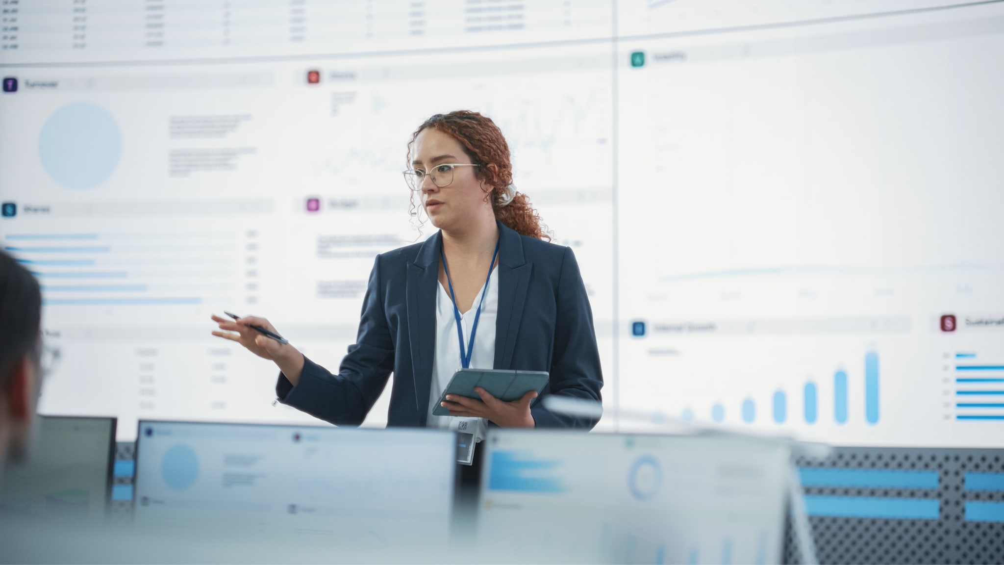 Woman standing in front of a screen with graphs, giving a presentation.