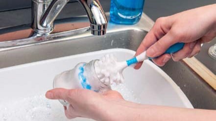A person washing a bottle with a scrub brush.