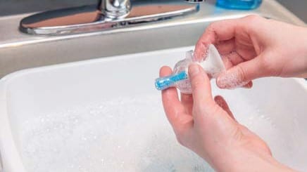 A person squeezing soapy water through a bottle nipple.