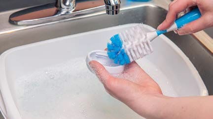 A person cleaning bottle cap with scrub brush.