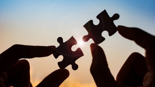 A person connecting two puzzle pieces with sun in the background