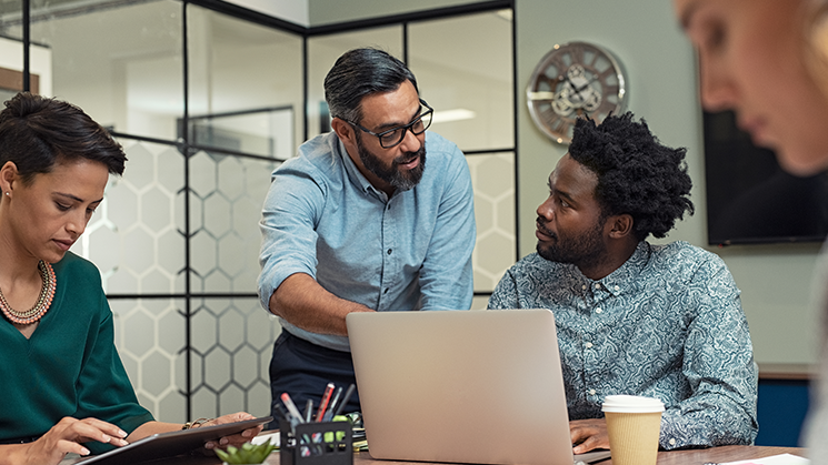 Two women and two men sitting around an office table working together. Two of them are discussing with an open laptop.