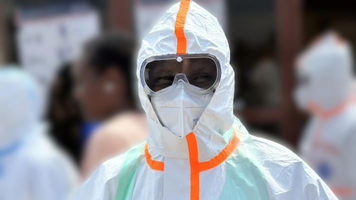 Person wearing full personal protective equipment for viral hemorrhagic fevers, including face mask, goggles, and hood.