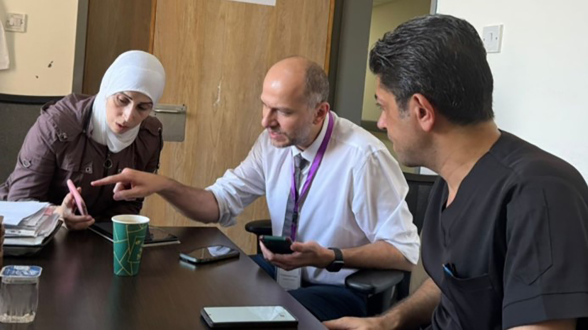Three staff members sitting at a long table in an office have a discussion.
