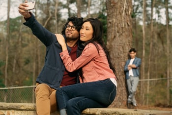 Couple taking a picture while a man watches in the background.