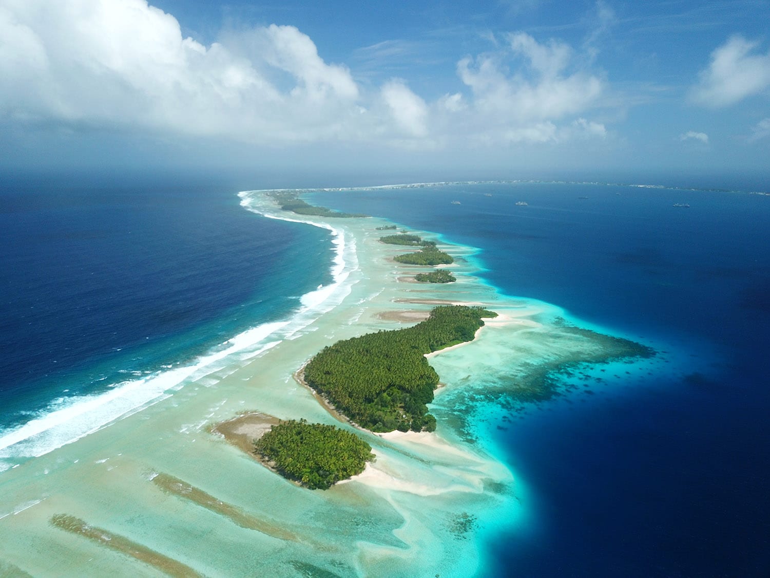Aerial view of a narrow tropical island with lush greenery surrounded by vibrant turquoise waters and coral reefs.