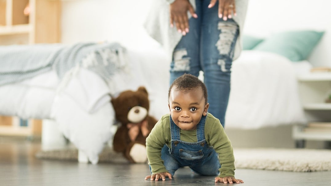 Small black male toddler crawling on floor towards the camera.