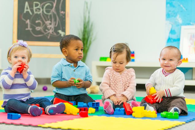 Two toddler boys and two toddler girls play with toys in a preschool classroom.