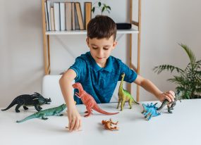 Young boy playing with toy dinosaurs on a table.