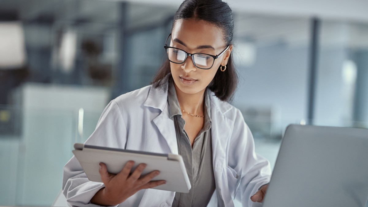 A female researcher refers to her tablet while working on her computer.