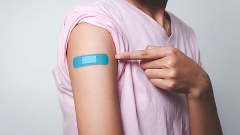 Young person pointing to an adhesive bandage on her arm after injection of vaccine.
