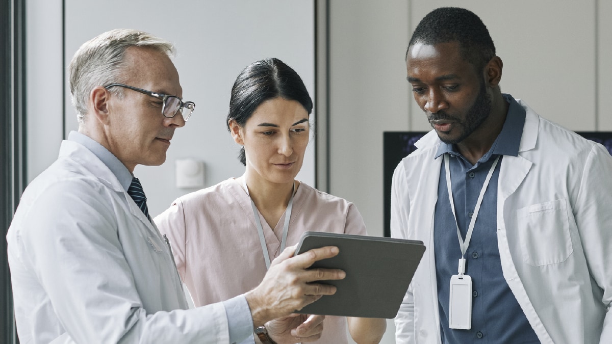 The image shows three clinicians looking at a tablet.