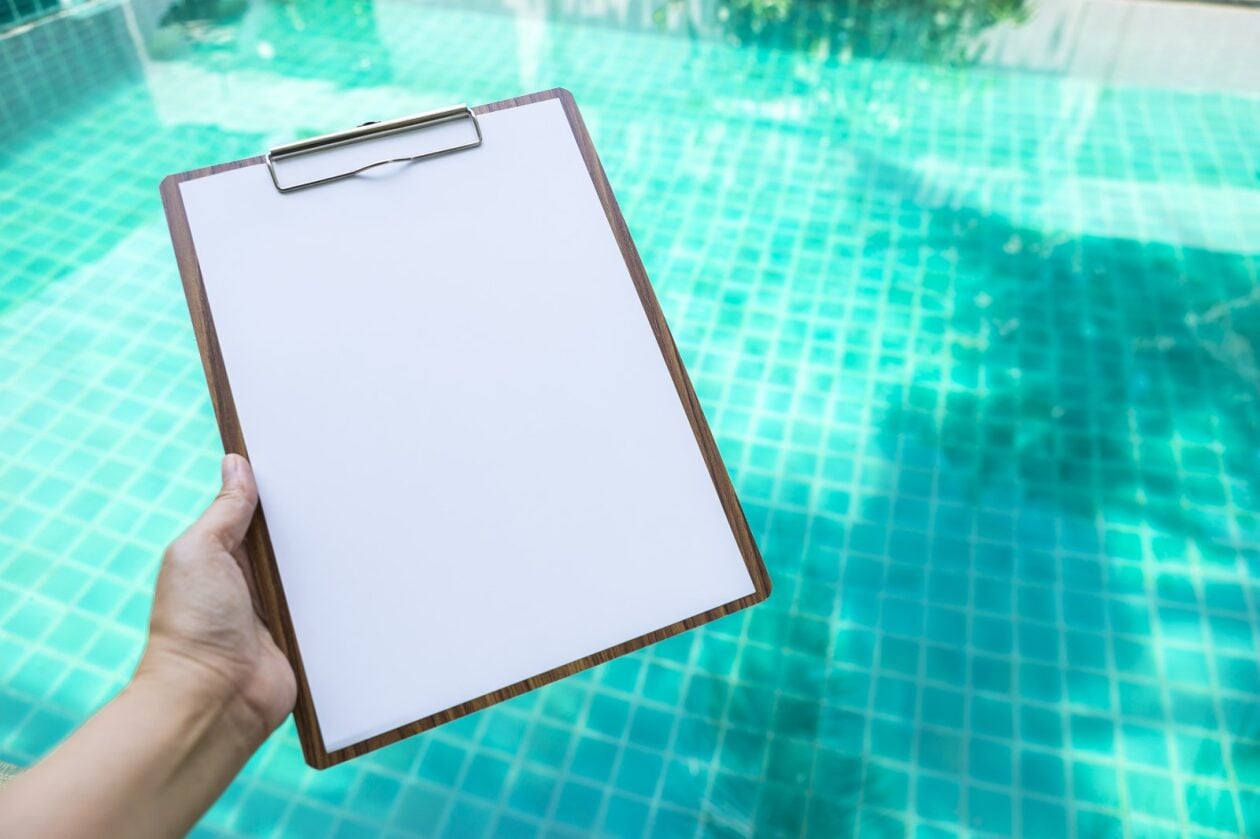 A hand extended over a pool holding a clipboard.