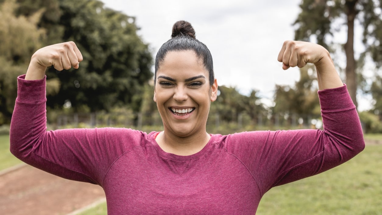 Woman smiles as she flexes her biceps.