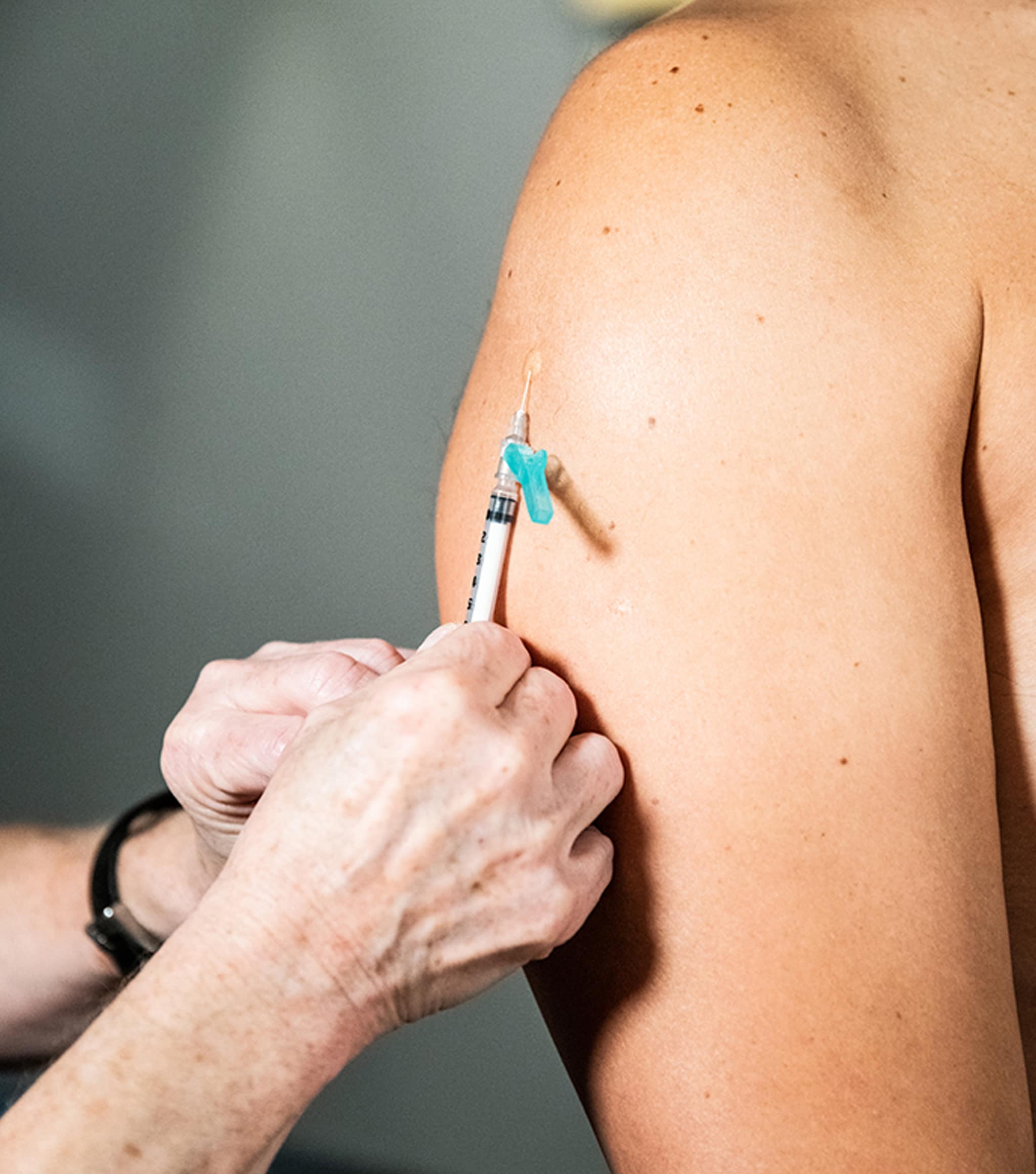 Image of a hand inserting a vaccination into a light-skinned person's deltoid.