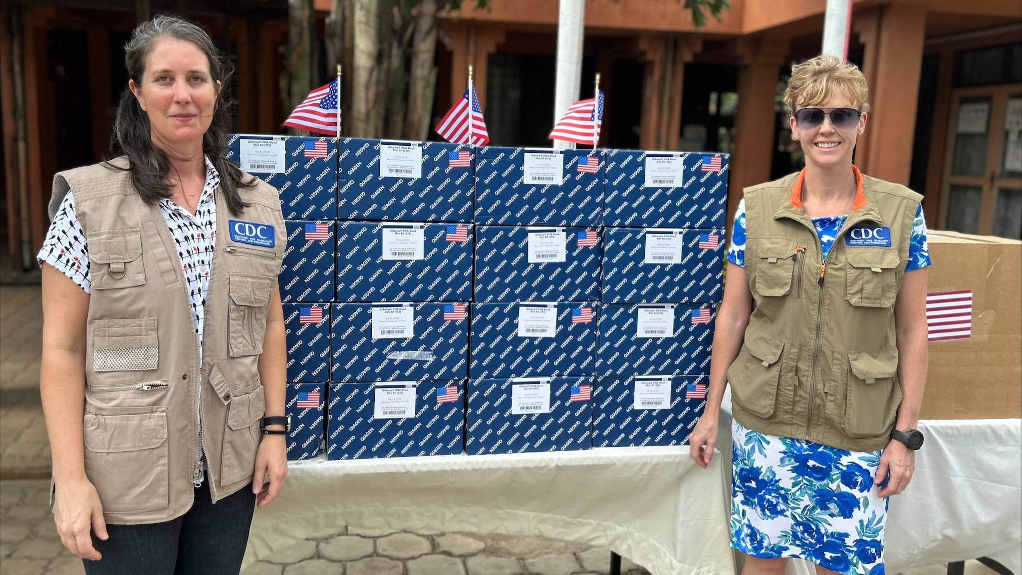 two women stand by a table covered in boxes, which contain laboratory testing supplies for mpox