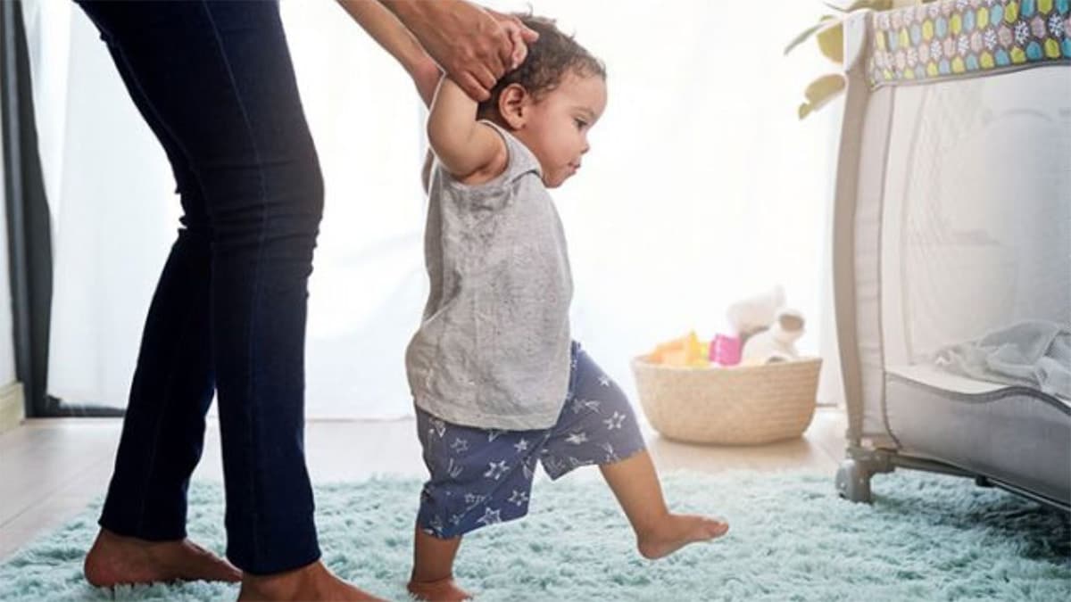 A mom holds hands and helps her child take their first steps