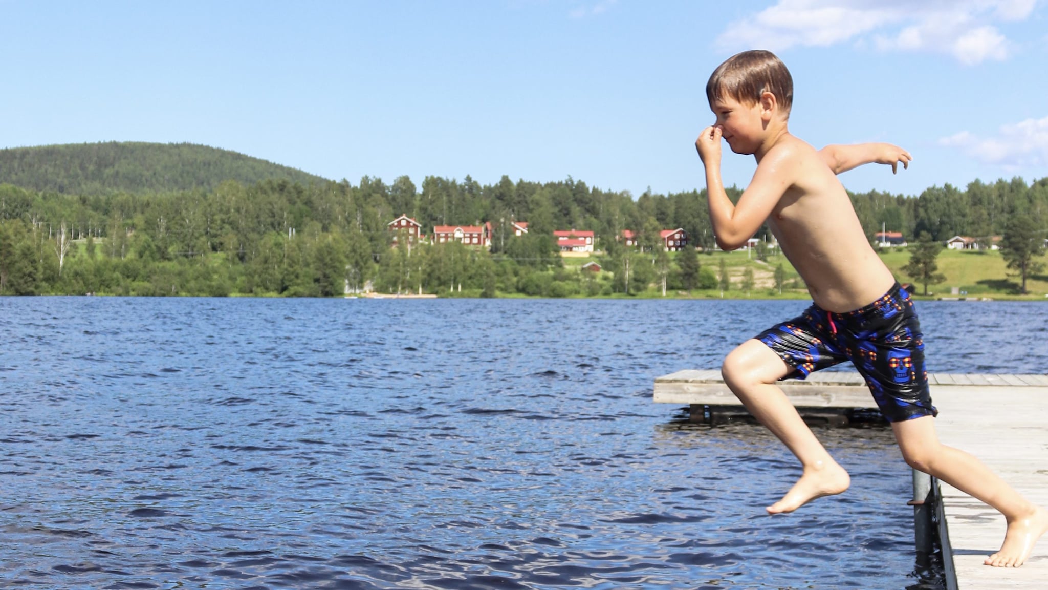 Young boy holds his nose jumping off a dock into a lake