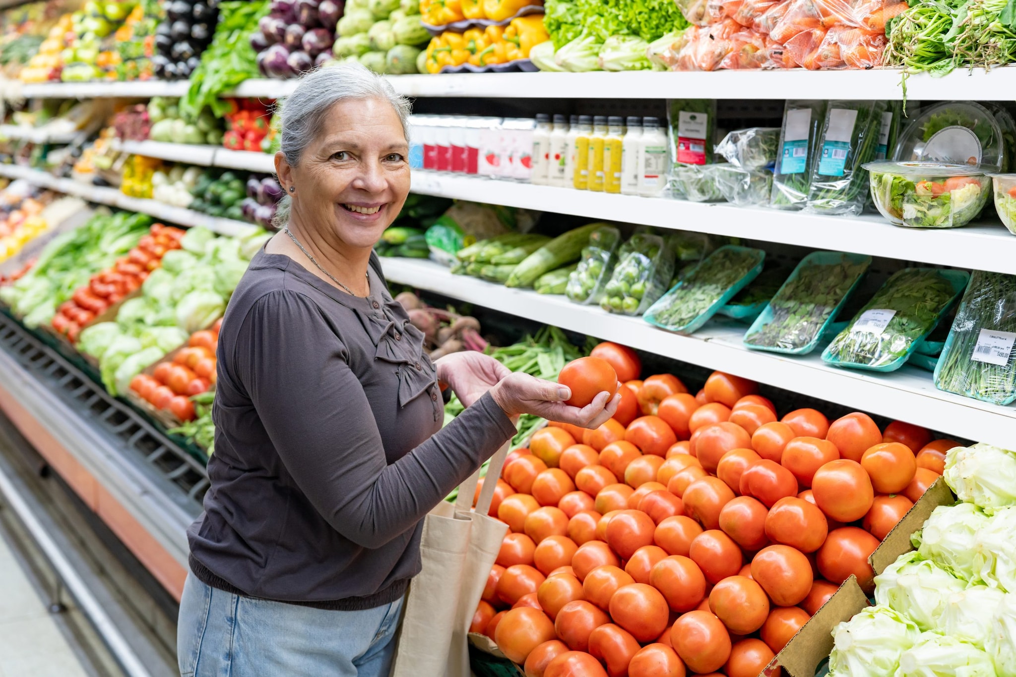 Woman looking at the camera while holding a tomato in the produce section of the grocery store.