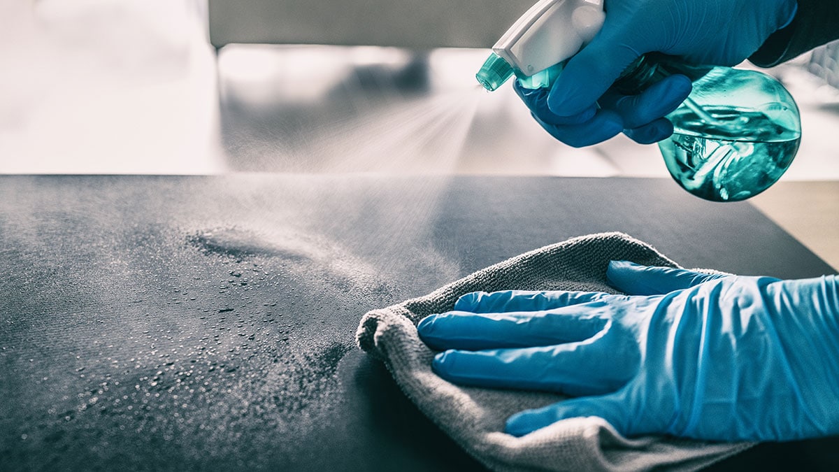 Person wearing cleaning gloves, spraying and wiping a flat surface.