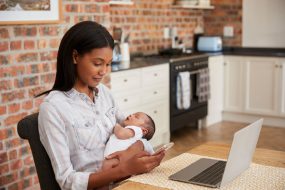 Get an Evaluation Mother Working On Laptop Holds Newborn Son And Sends Text