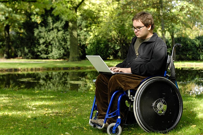 Man in a wheelchair reading his laptop