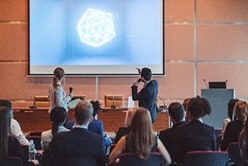 Two speakers giving a talk in a conference with people sitting in audience.