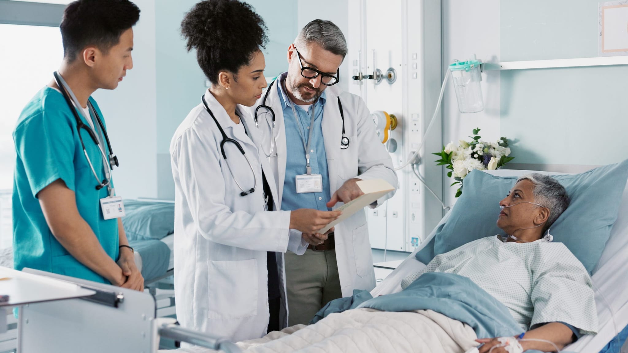 Two male doctors and a female doctor next to a patient's bed in a hospital