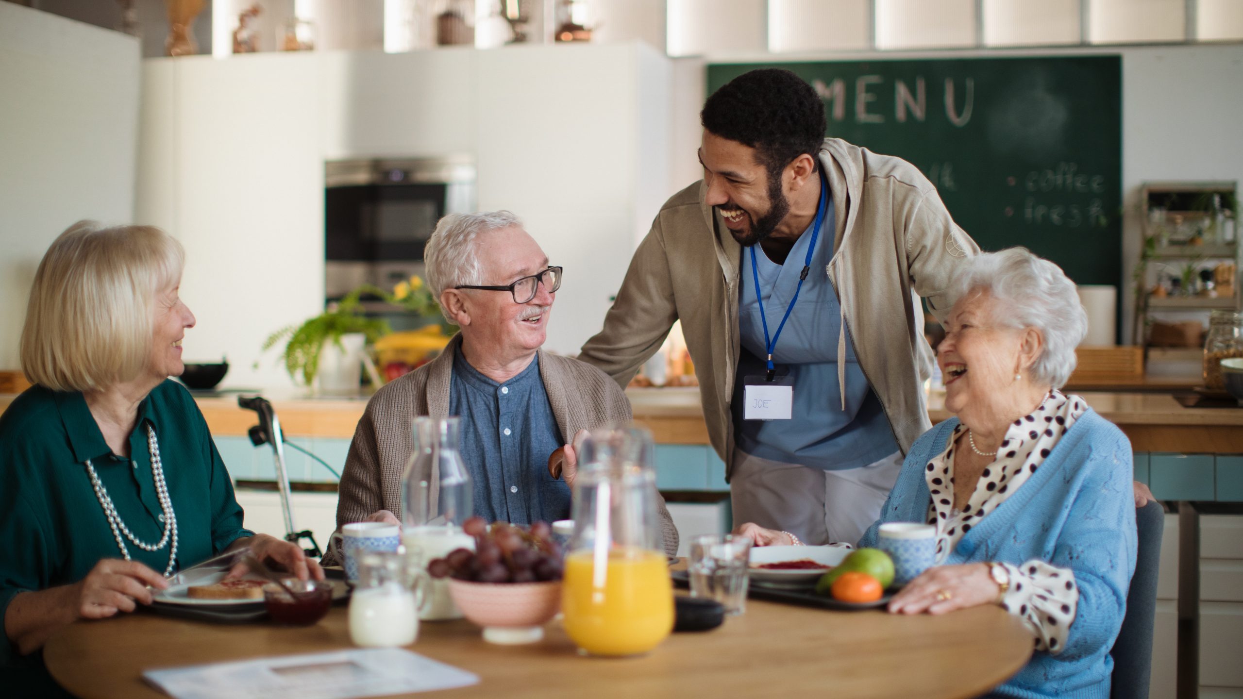 Group of seniors talking to a male healthcare worker while eating in a cafeteria