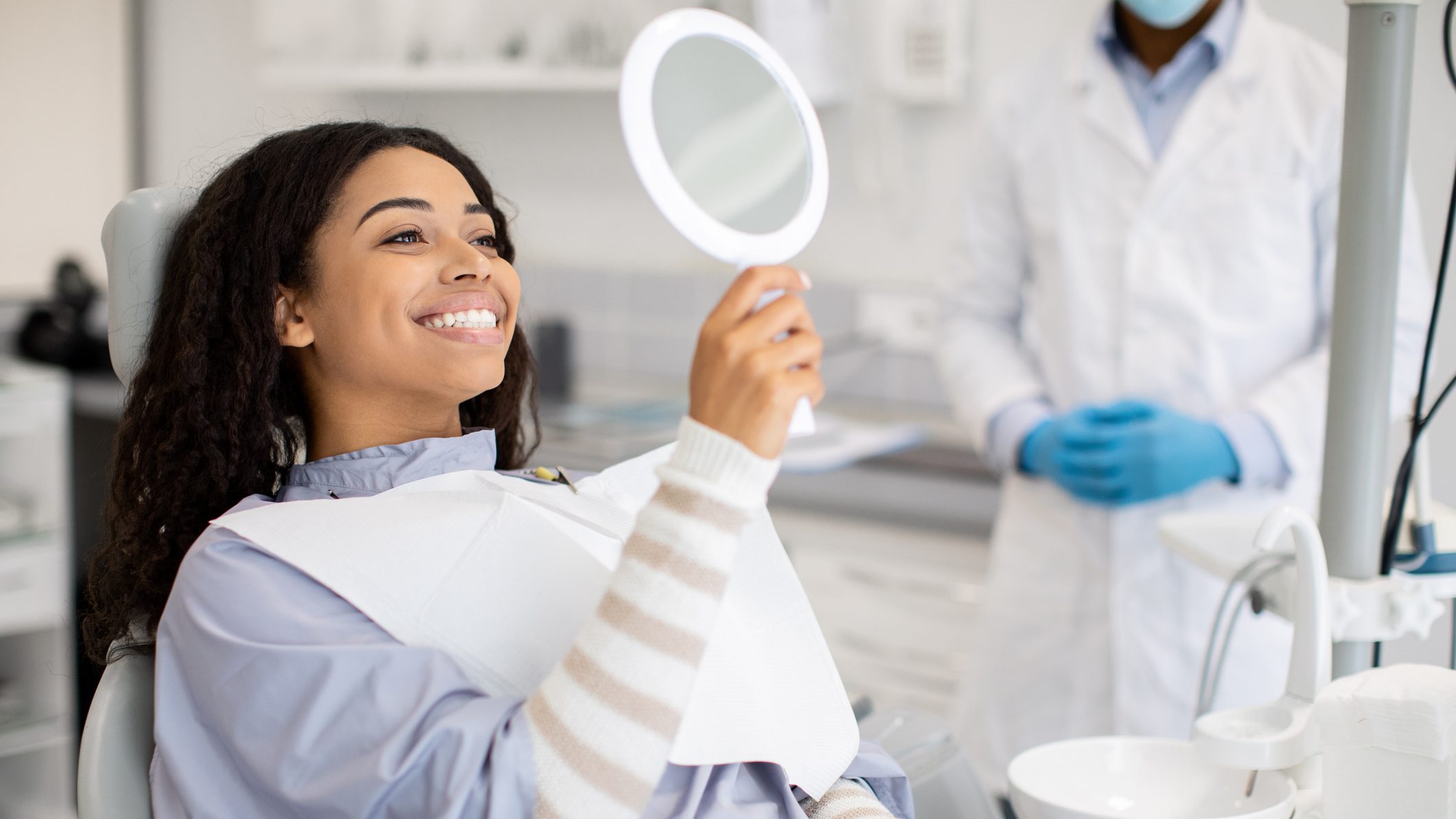 Happy Black Female Patient Looking At Mirror After Dental Treatment In Clinic