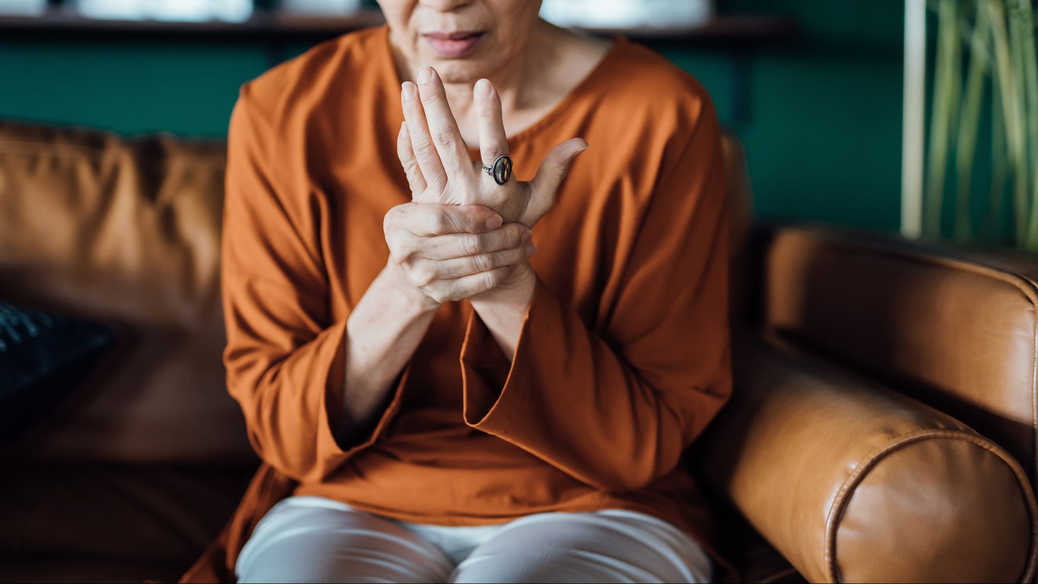 Senior woman rubbing her hands in discomfort, suffering from arthritis in her hand while sitting on sofa at home. Elderly and health issues concept