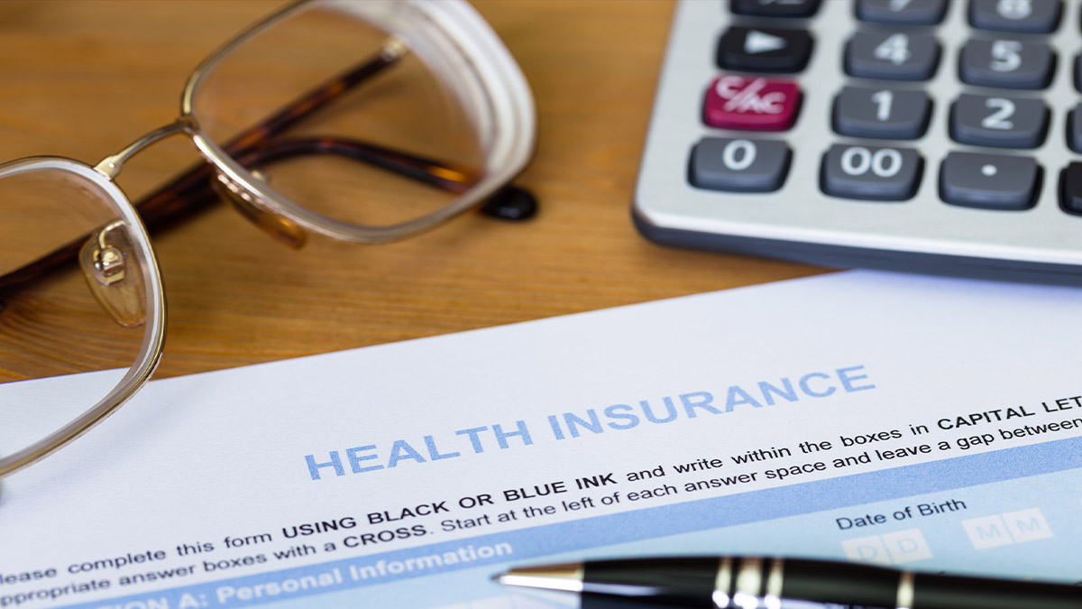 A form reading Health Insurance on a table with a pen, calculator, and glasses