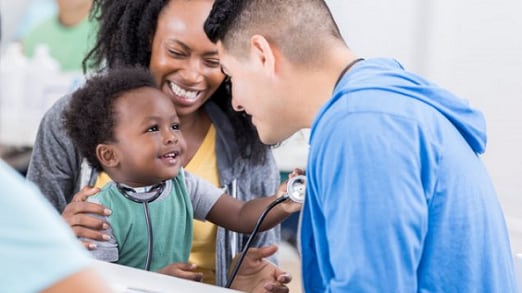 Young black mom and toddler. Toddler holds a stethoscope to an Asian provider's chest.