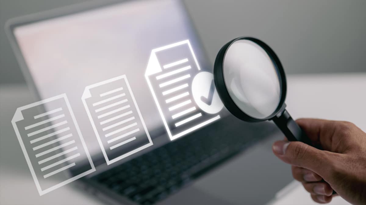 Conceptual image of hand with magnifying glass reviewing documents