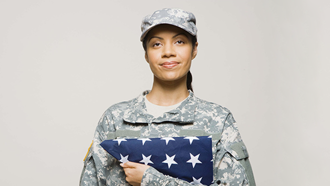 Image shows female veteran in camouflage uniform holding folded flag