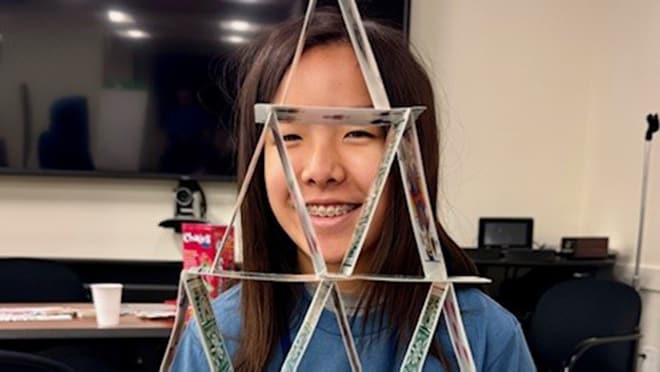 Young asian girl stands behind a house triangle formed by balancing playing cards