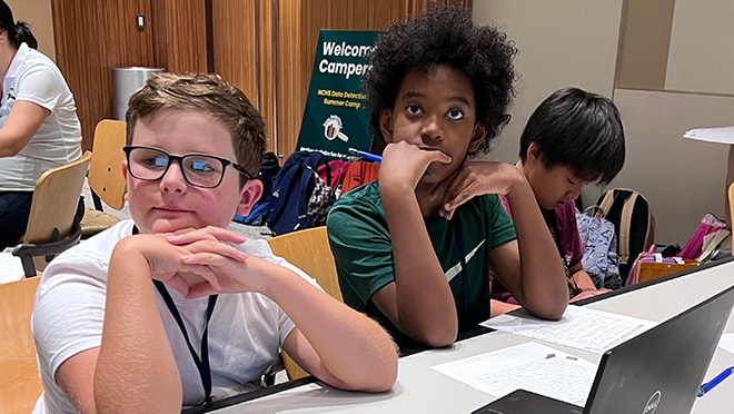 Campers sit at a table, listening intently to an instructor