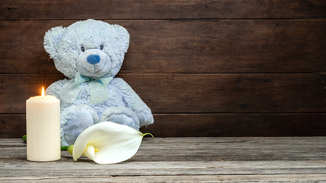 A teddy bear sitting on a table next to a lit candle and a white flower.