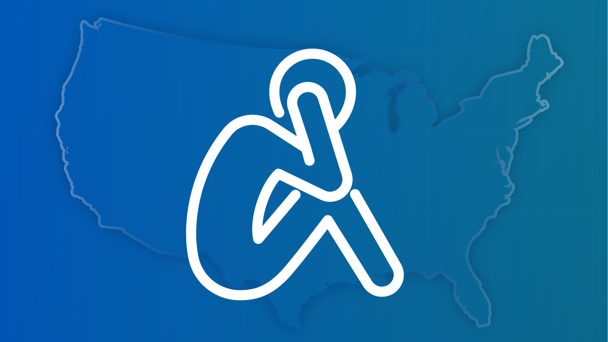 An outline of a person, set against  a U.S. map, with their knees to their chest and holding their head.