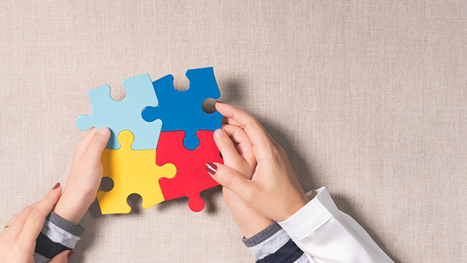Top view of mother's hands holding young child's hands holding colorful jigsaw puzzles on beige linen cloth.