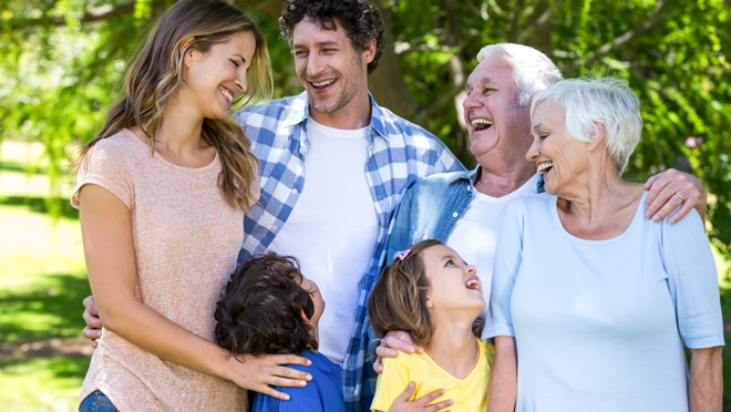 A multi-generational family laughing together and hugging. Two kids, two adult parents, and two elderly grandparents.